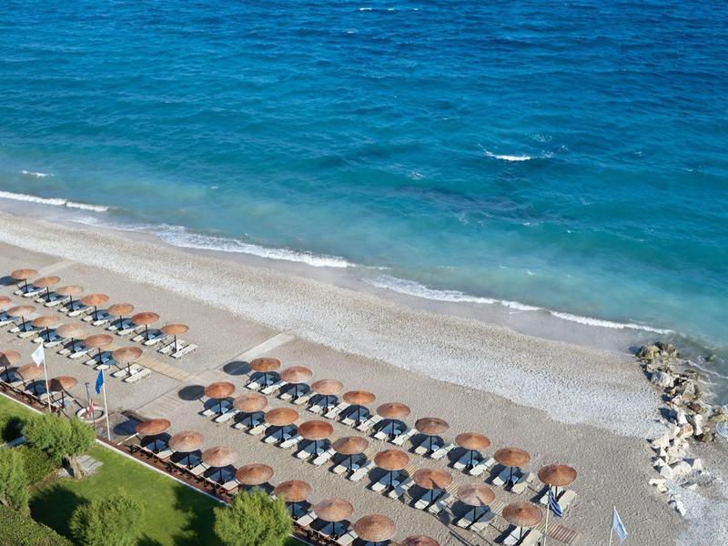 Beach with rows of sun umbrellas and lounge chairs by clear blue sea