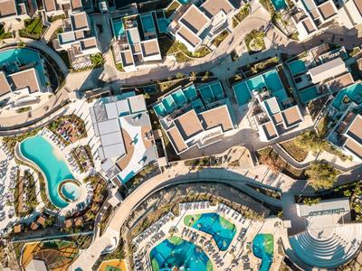Aerial view of a resort with multiple pools, buildings, and pathways in a sunny landscape.