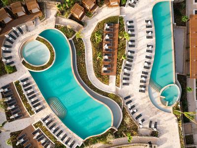 Aerial view of a curvy swimming pool with sun loungers and small cabanas in a resort.
