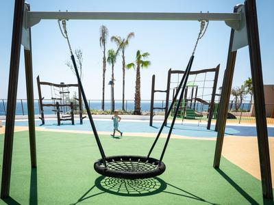 Modern circular swing on green flooring with palm trees and blue sky by the beach