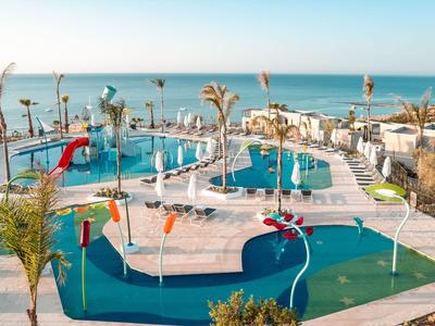 Moderner Hotelpool mit Wasserrutschen und Palmen am Mittelmeerstrand.