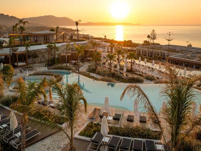 Hotelpool mit Liegestühlen und Palmen bei Sonnenuntergang am Meer.