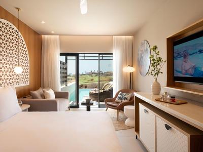 Modernes Hotelzimmer mit Kingsize-Bett, Sitzbereich und offenem Balkon mit Meerblick.