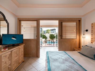 Hotelzimmer mit Doppelbett, Holzmöbeln und Blick auf einen Pool durch offene Türen.