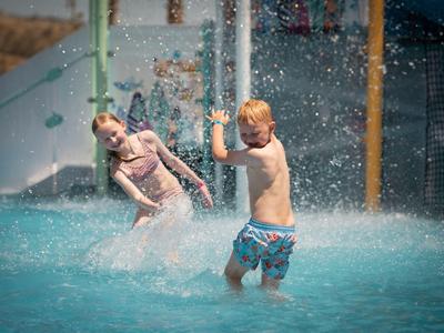 Kinder spielen fröhlich in einem Wasserpark mit Wasserstrahlen und spritzendem Wasser.
