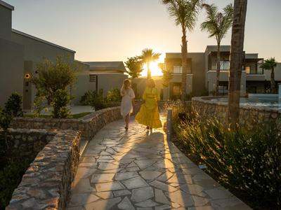 Zwei Frauen gehen auf einem gepflasterten Weg bei Sonnenuntergang in einem Hotelresort.
