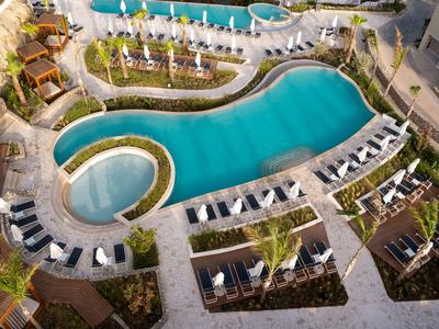 Luftaufnahme eines Hotelschwimmbads mit Liegestühlen und Palmen rundherum.