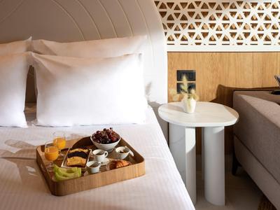 Frühstückstablett mit Speisen auf einem weißen Hotelbett neben einem modernen Nachttisch.