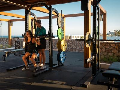 Person trainiert unter Anleitung im Freiluft-Fitnessstudio mit Sonnenuntergang im Hintergrund.