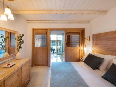Helles Hotelzimmer mit Doppelbett, Holzmöbeln und Blick auf Balkon bei Tageslicht.
