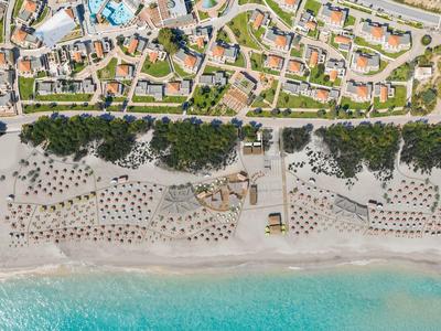 Luftaufnahme eines Strandes mit Sonnenschirmen, Liegen und angrenzenden Gebäuden.