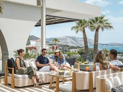 Terrasse mit moderner Outdoor-Möblierung, Palmen und Blick auf Hügel und Gebäude.