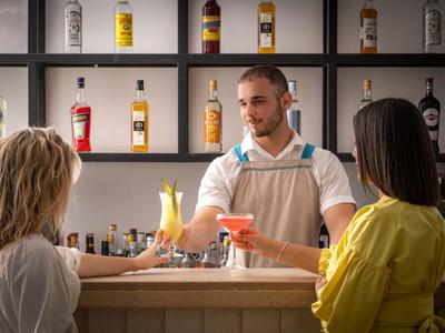 Zwei Frauen an einer Hotelbar bekommen Cocktails von einem Barkeeper serviert.