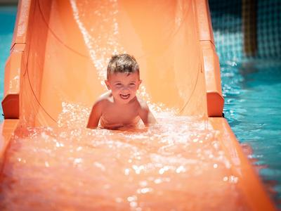 Ein Kind rutscht lächelnd eine orange Wasserrutsche in einem Pool hinunter.