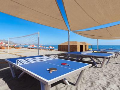 Sandstrand mit blauem Tischtennis- und Liegestühlen unter Sonnensegeln am Meer.