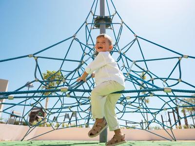 Ein Kind klettert auf einem blauen Netzspielplatz unter klarem Himmel im Freien.