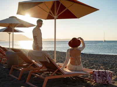 Personen entspannen sich auf Liegestühlen am Strand unter Sonnenschirmen bei Sonnenuntergang.