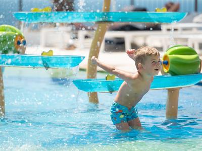 Junge spielt in einem Wasserpark mit blauen Wasserspielen und spielt mit Wasserstrahlen.