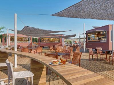 Moderner Außenbereich eines Hotels mit Bar, Holzboden und sonnigen Sitzbereichen unter Segeln.