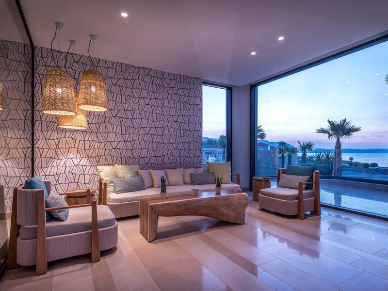 Luxury lounge area with panoramic windows overlooking the sea at sunset.