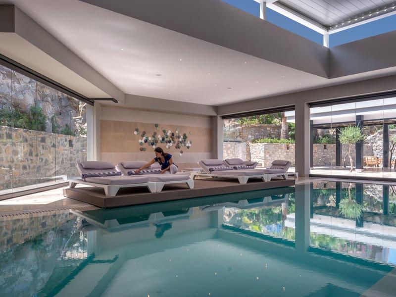 Modern indoor pool with daylight, loungers, and view of stone walls in hotel