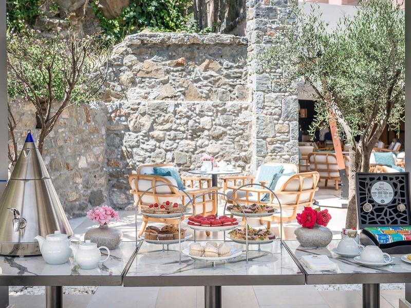 Buffet with tea, pastries, and snacks in front of a stone wall and outdoor chairs