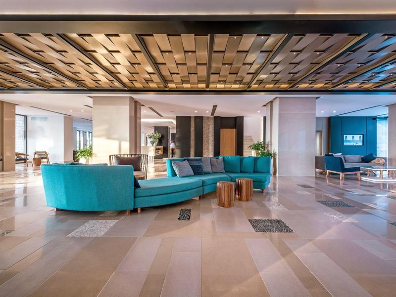 Modern hotel lobby area with blue sofa, wooden table, and decorative ceiling.