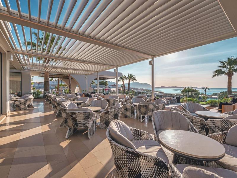 Covered restaurant terrace overlooking the sea and palm trees at sunset.