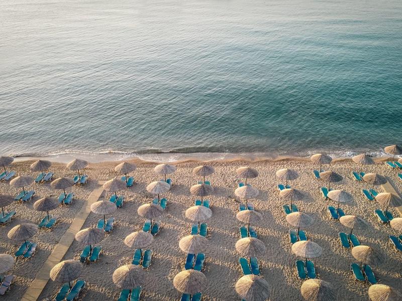 Aerial view of a beach with evenly spaced sun umbrellas and loungers by calm sea.