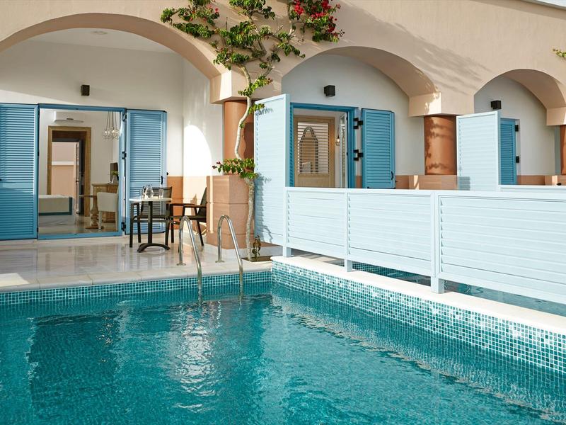 Hotel terrace with blue pool and seating area in front of white arches and blue doors.