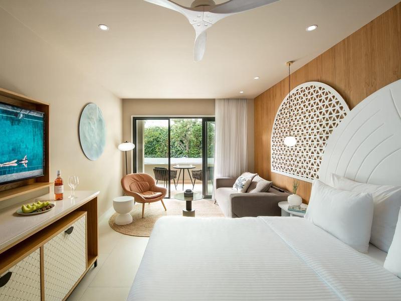 Modern hotel room with large bed, seating area, and view of terrace with garden.