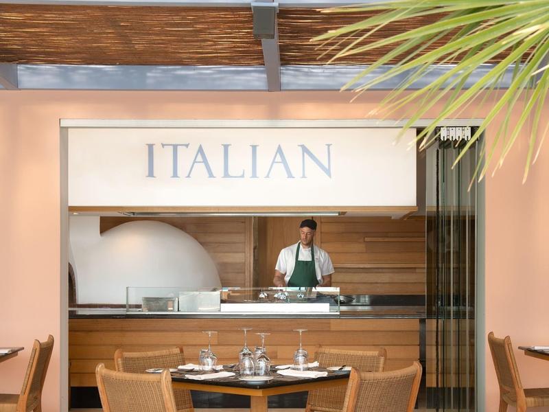 Modern Italian restaurant area with wooden furniture and open kitchen under a bamboo roof
