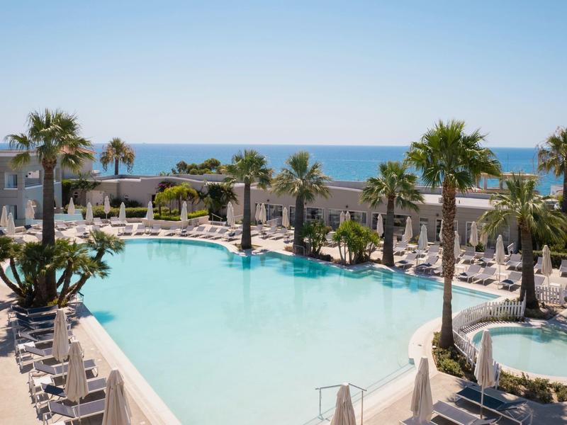 Large outdoor pool with sun loungers and palm trees by the sea.