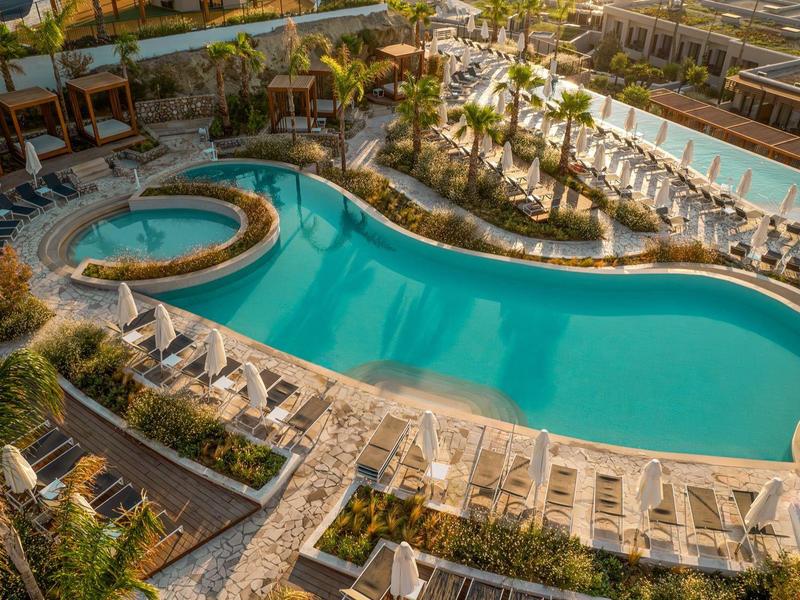 Curved pool with palm trees, sun loungers, and sea view at sunset.