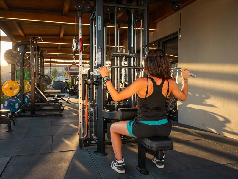 Woman working out on a fitness machine in a well-lit gym with wooden beam ceiling.