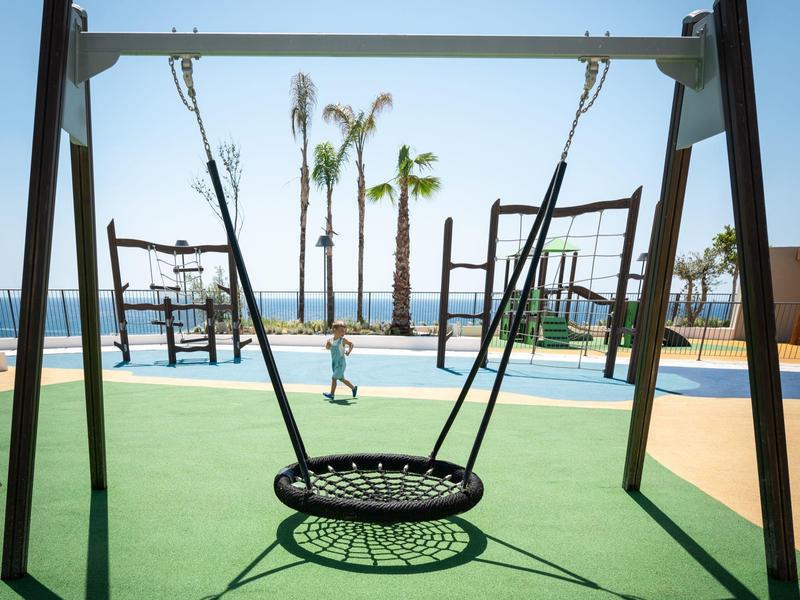 Modern circular swing on green flooring with palm trees and blue sky by the beach