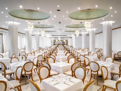Spacious, elegant banquet hall with round-backed chairs and tables set for dining.