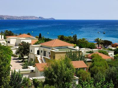 Coastal resort with villas, greenery, and a clear blue sea in the background.
