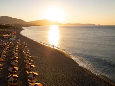 Strand mit Sonnenschirmen und ruhigem Meer bei Sonnenuntergang an einem Hotelstandort.