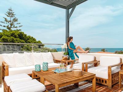 Elegante Terrasse mit weiß gepolsterten Sesseln und Holztisch mit Blick aufs Meer.