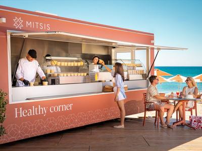 Outdoor-Stand mit gesunden Snacks und Getränken neben Strand mit Sonne und Gästen.