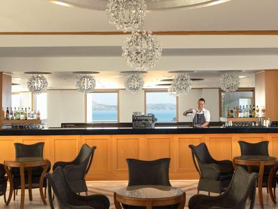 Helle Hotelbar mit runden Holztischen, schwarzen Stühlen und modernen Kronleuchtern.