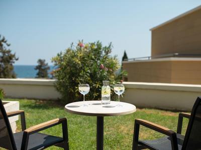 Zwei Stühle und ein Tisch mit Getränken auf einer Terrasse mit Meerblick bei klarem Himmel.