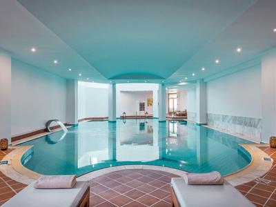 Hell beleuchteter Indoor-Pool mit Liegestühlen und weiß getünchten Wänden in einem Hotel.
