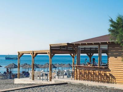 Wooden beach bar by the sea with tables, chairs, and straw umbrellas on a sunny day.