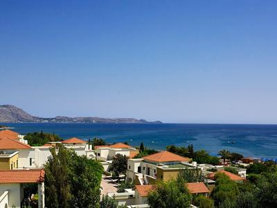 Coastal village with red-roofed houses and blue sea under clear sky.