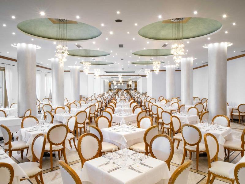 Spacious, elegant banquet hall with round-backed chairs and tables set for dining.