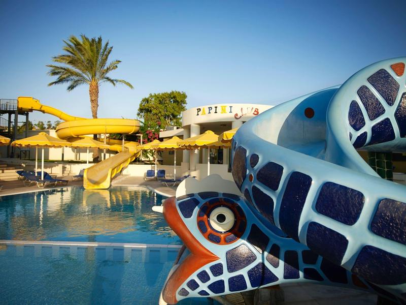 Waterpark area with slides and fish-themed structure by a pool under clear blue sky.