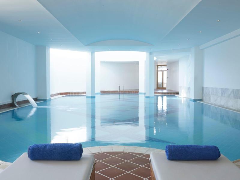 Indoor pool with white walls, tiled floor, and two blue towels on the edge.