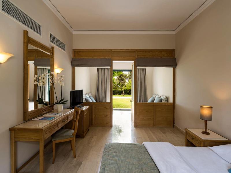 Cozy hotel room with wooden furniture and a view of a green garden through the open doors.